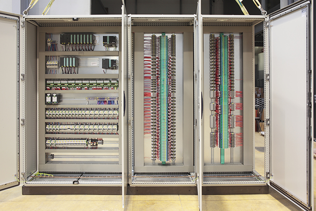 An open building-controls cabinet with terminal strips, relays and loomed wiring