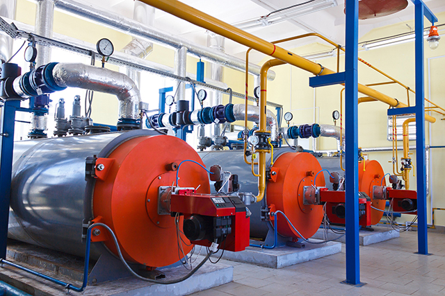 Three orange-fronted boilers with insulated heating-water pipework and gauges in a plant room