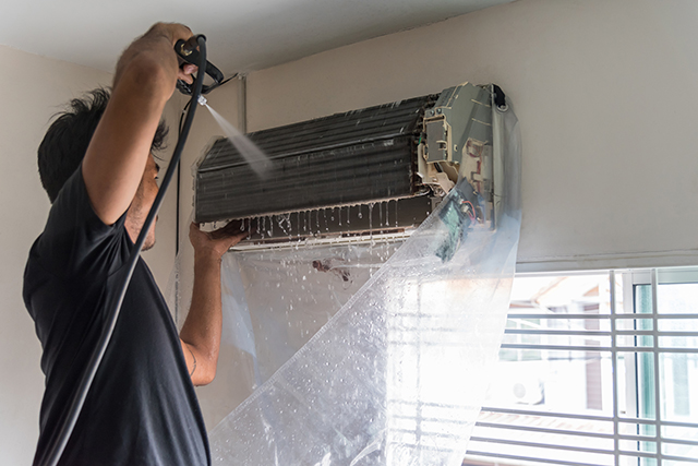 A technician washing a wall-split indoor coil, with the unit bagged to catch the water