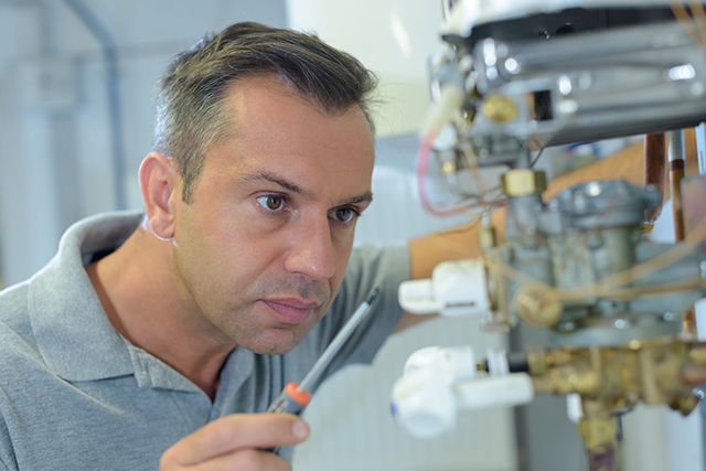 A technician inspecting the gas valve and pipework on a heating appliance