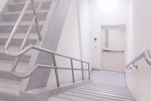 A concrete fire stair with metal handrails and a fire door at the landing
