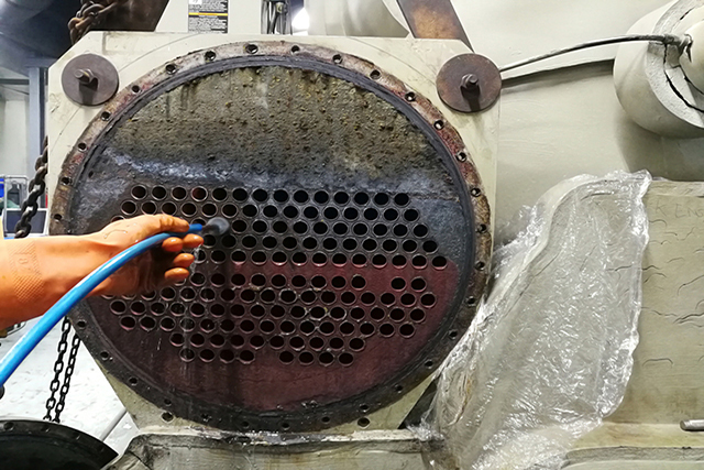 A gloved hand hosing a fouled chiller tube plate during a tube clean